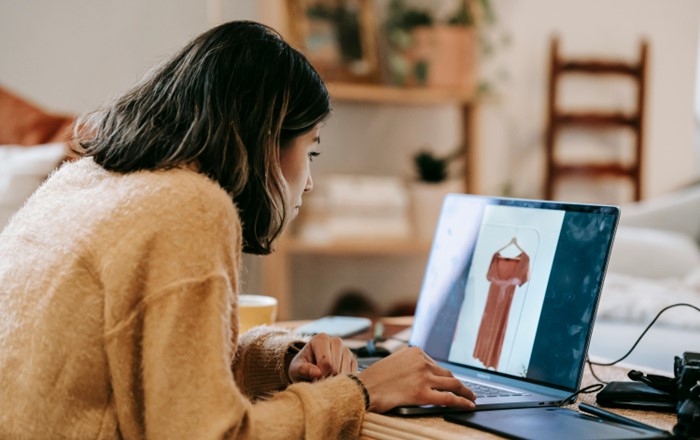 A woman sits in front of a laptop screen which shows a dress
