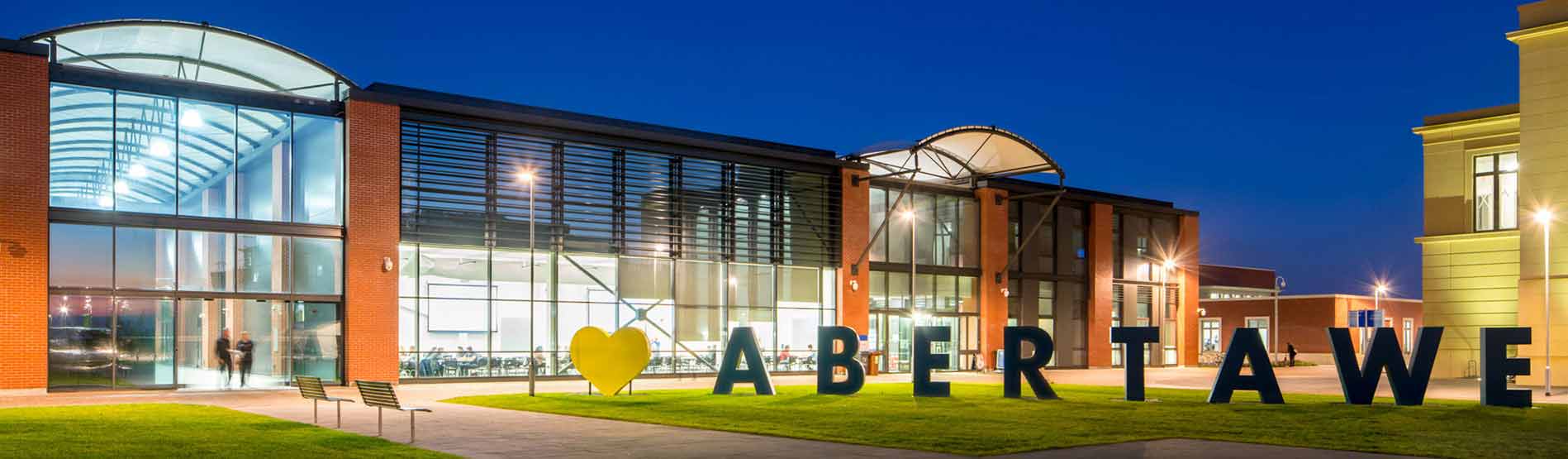This image was taken at night time. The College of Engineering is lit up. There is a large sign outside which reads 'I love Abertawe'. Abertawe is Welsh for 'Swansea.