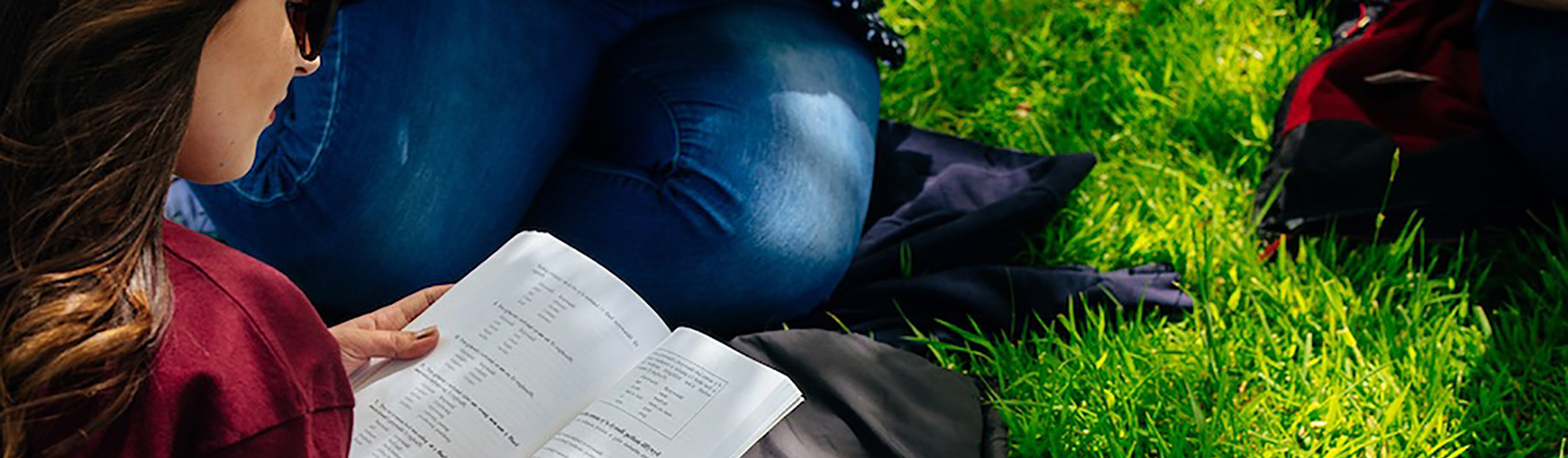 Student reading whist sitting on grass
