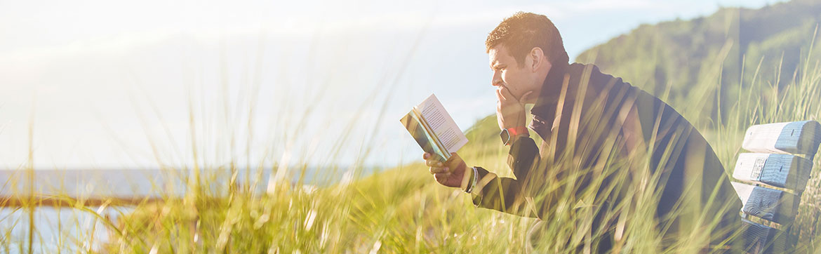 A man reading a book on a coastal bench