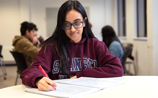 A person in a red Swansea University hoody revising.