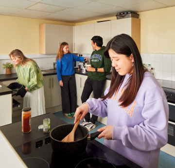 An image of four students cooking and talking in a shared kitchen in student accommodation on Singleton Campus.