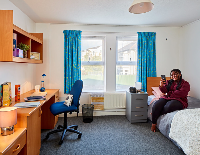 Female student sitting on bed looking at smartphone.