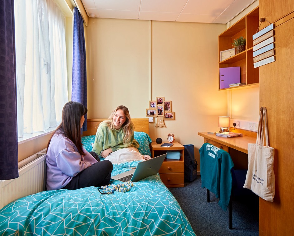 A university bedroom with two students chatting.