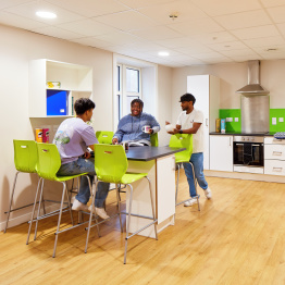 A group of three students talking in the kitchen in student accommodation on Bay Campus.