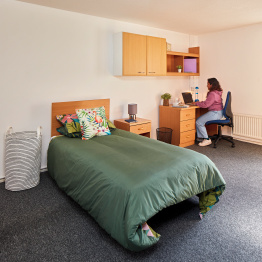 An image of a student working at a laptop in a room in student accommodation.