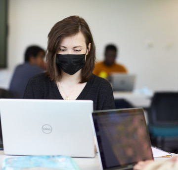 a female student on a laptop wearing a mask