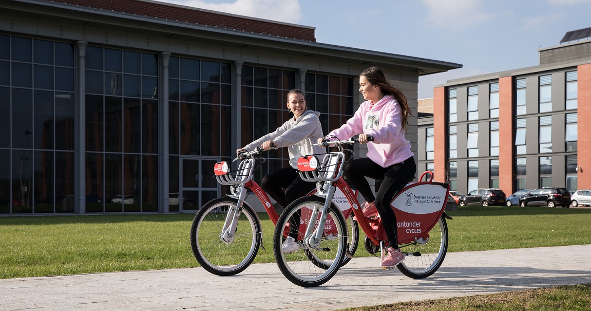 2 female students riding bikes on the Bay campus