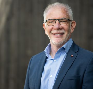 Man wearing a suit standing against a black background smiling at the camera