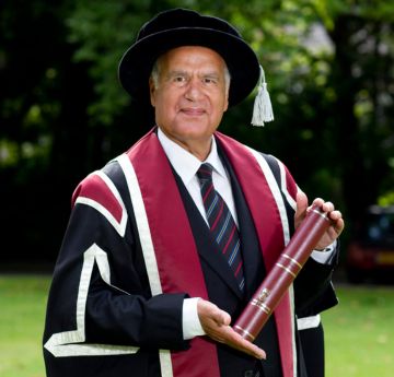 Man in cap and gown standing outdoors smiling at the camera