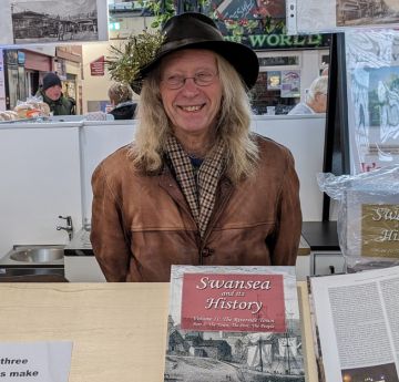 Man sitting at a desk surrounded by books smiling at the camera