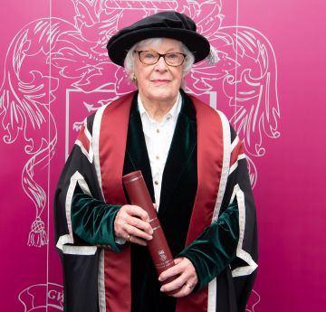 Lady standing with cap and gown in front of a backdrop smiling for a photo