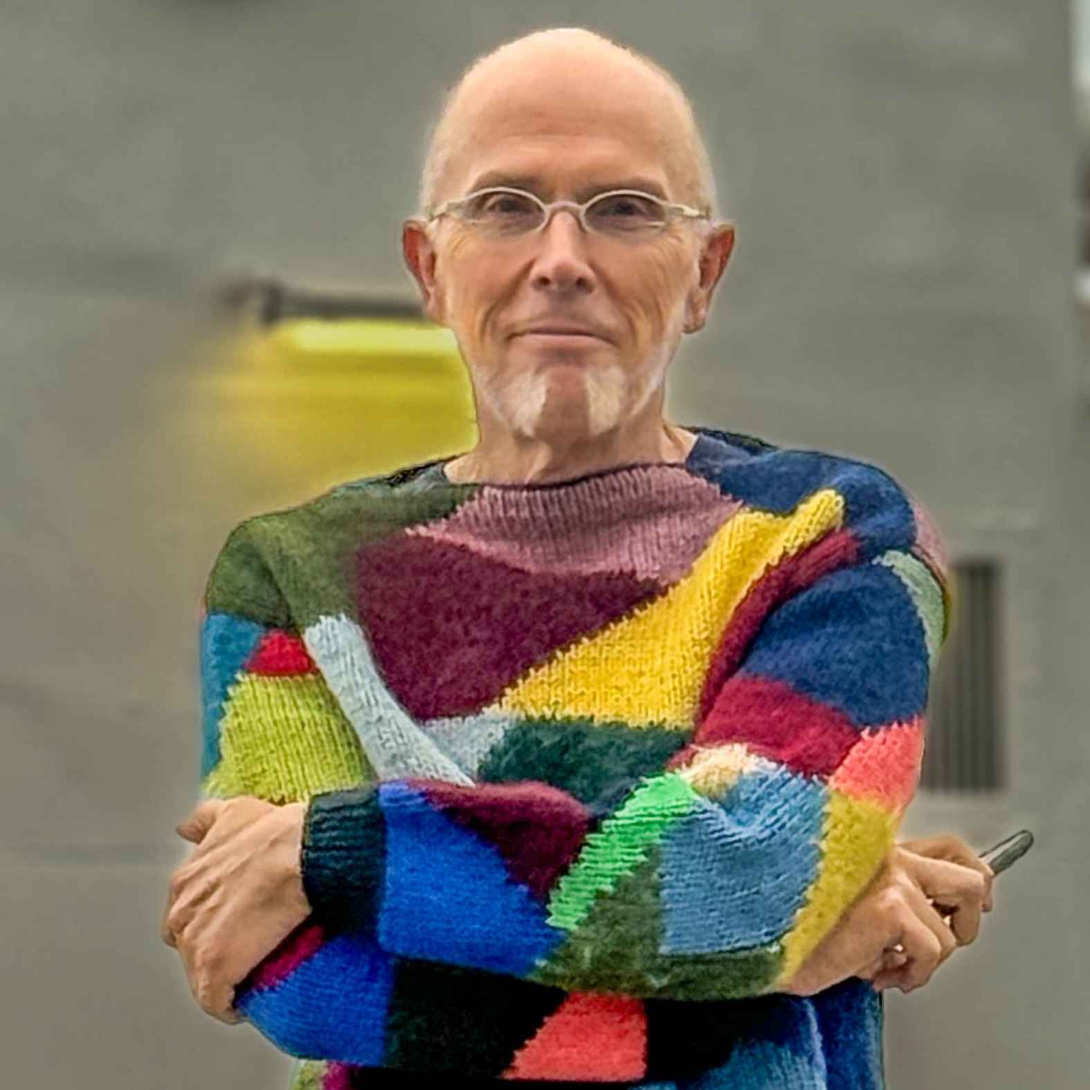 Man wearing a colorful knitted jumper folding his arms smiling at the camera