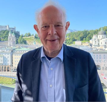 Man in a shirt and tie standing in front of a river smiling at the camera