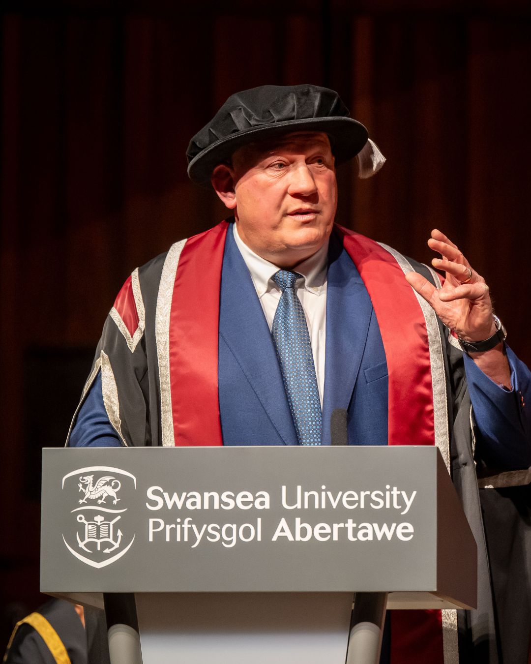 Man wearing cap and gown standing at a lectern giving a speech.