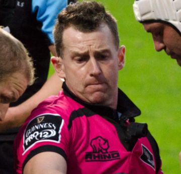 Man wearing a pink and black jersey refereeing a rugby match