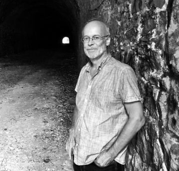 Man standing with his back on a wall with a tunnel behind him.
