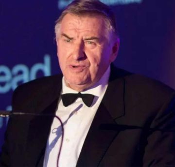 Man in a tuxedo making a speech at a lectern