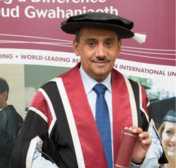 Man wearing cap & gown holding a scroll smiling at the camera