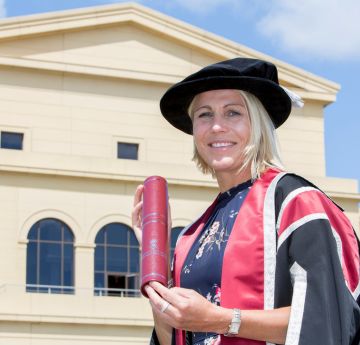 Lady in cap and gown standing in front of a great hall