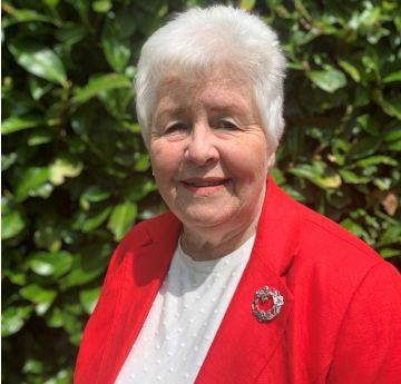 Lady wearing a red blazer and brooch standing in front of a busg