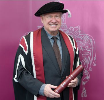 Man in cap and gown holding a scroll smiling at the camera