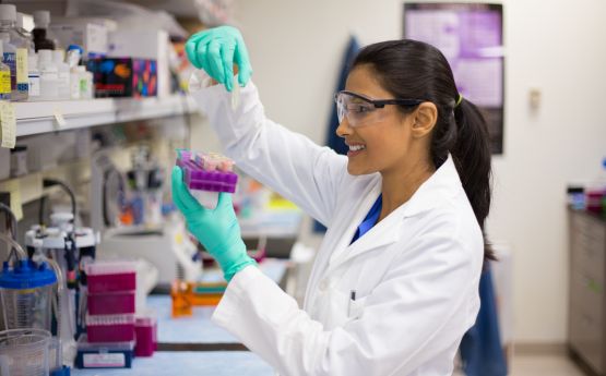Lady in a medical lab wearing a doctor's coat experimenting with test tubes