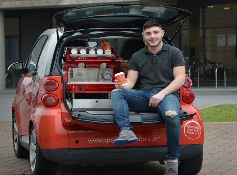boy sitting in the boot of a car with a coffee