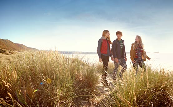 Three students walking through sand dunes on warm clothes at dusk