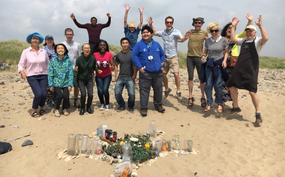 Image shows a group of students on the beach, gathered around collected plastic and rubbish.