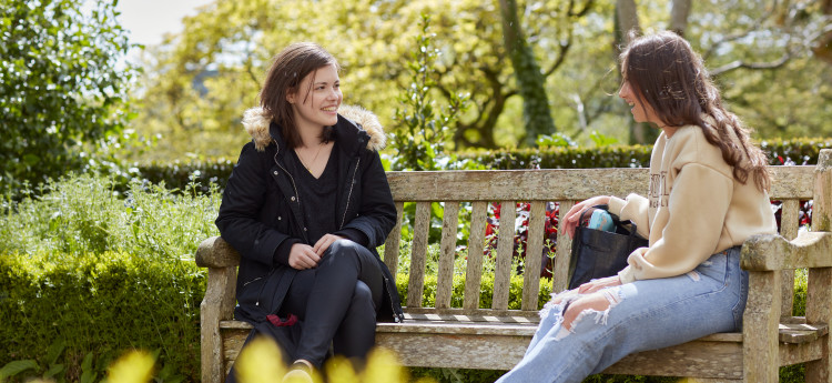 Two students sitting on a bench talking.