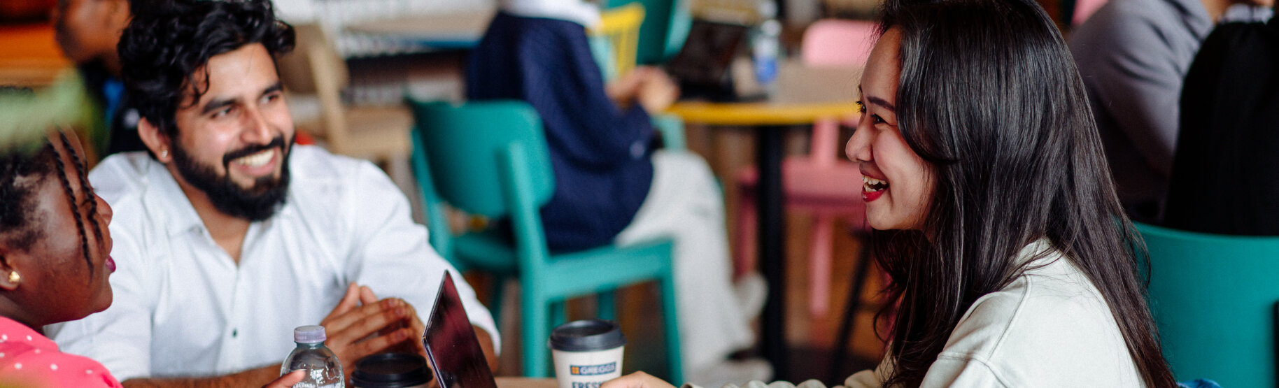 Students chatting at a table with coffee cups and laptops