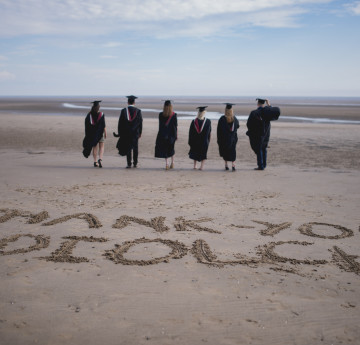 graduates walking across the beach, with Thank You/Diolch written in the sand