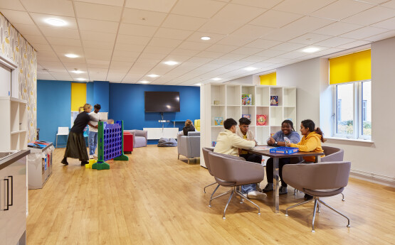 Students in their flat kitchen - one group sitting around a table whilst another play a large 'connect 4' game 