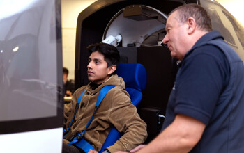 Student sitting in flight sim simulation with lab technician looking on