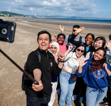 Tri myfyriwr yn eistedd i lawr ac yn bwyta bwyd