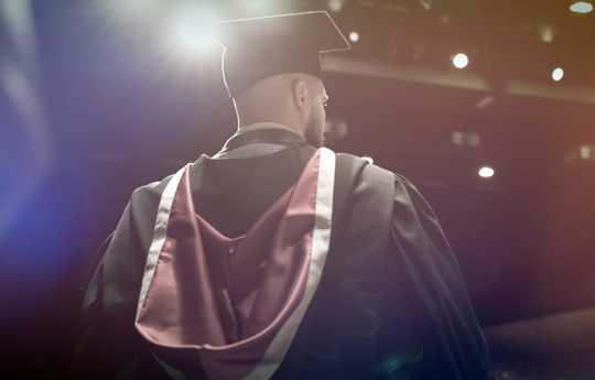 Cefn dyn mewn cap a gŵn graddio 