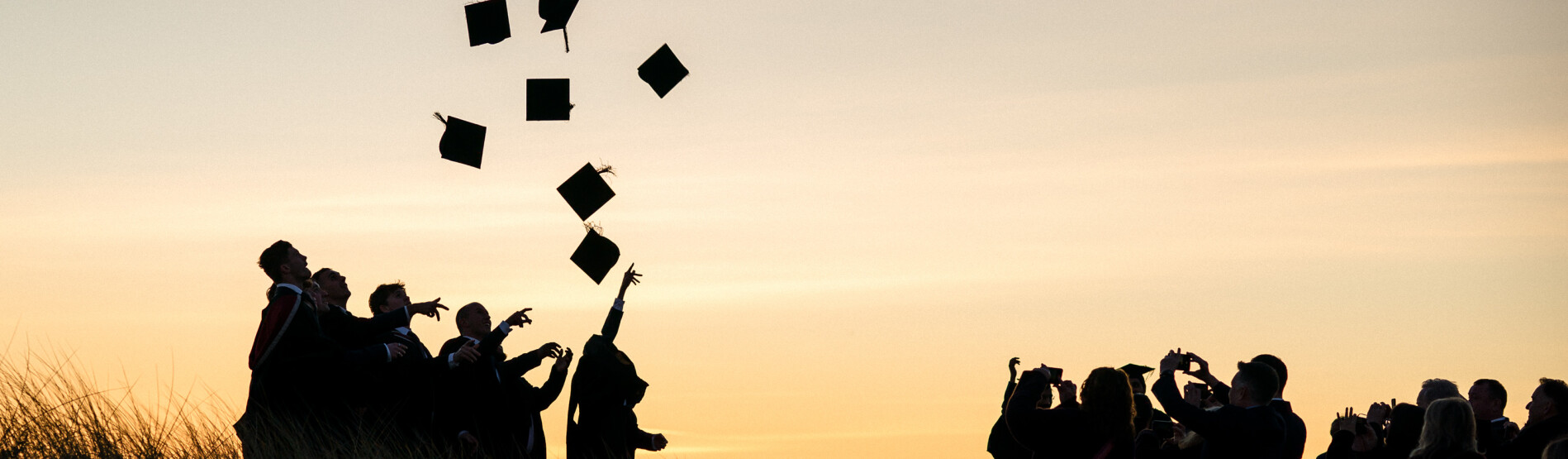 Image of students graduating, throwing hats up in the air on the beach 