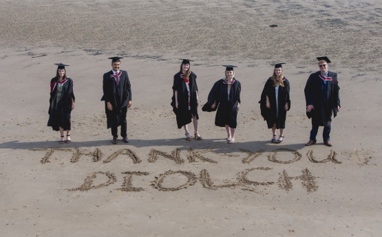 group of students standing over a thank you written in the sand