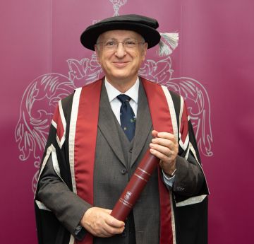 Dyn mewn gwisg graddio yn gwenu wrth y camera