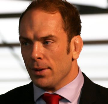 Dyn mewn crys a tei yn edrych i'r camera