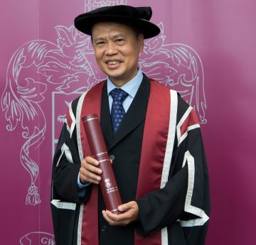 dyn mewn cap a gwn yn gwenu i'r camera