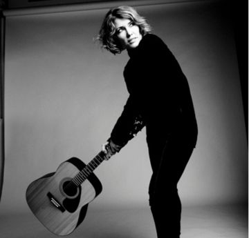 Menyw yn dal gitar yn edrych i ffwrdd o'r camera