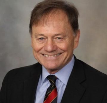 Dyn mewn siwt yn gwenu at y camera