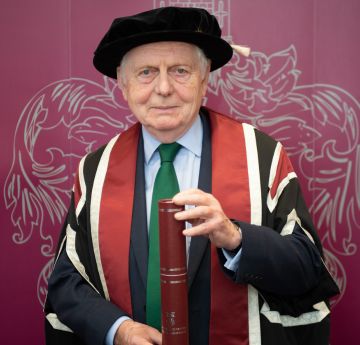 Dyn mewn gwisg graddio yn edrych i'r camera