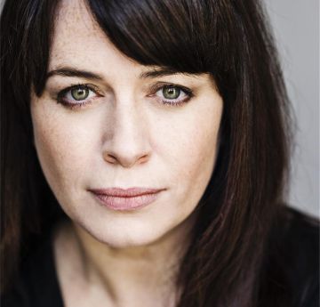 Menyw gyda gwallt du yn gwenu i'r camera