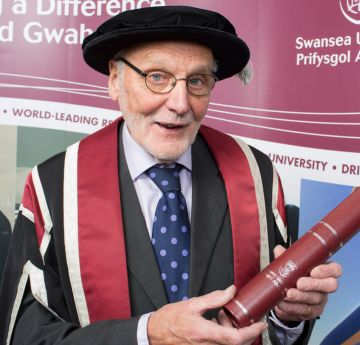 Man with a cap and scroll smiling at the camera