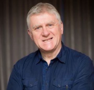 Dyn mewn crys yn gwenu wrth y camera