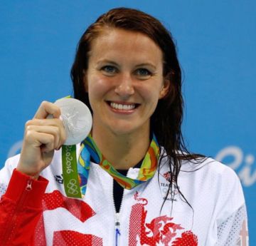 Lady holding up an Olympic medal smiling at the camera
