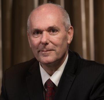 Dyn mewn siwt a tei yn gwenu i'r camera